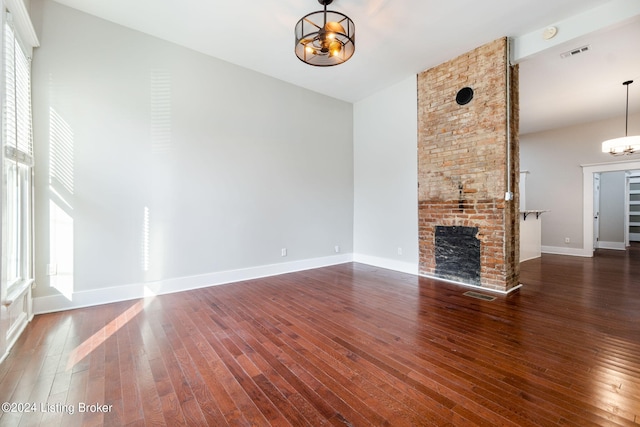 unfurnished living room with a fireplace, dark wood-type flooring, and an inviting chandelier