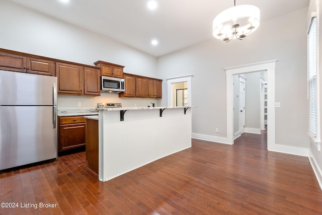 kitchen with hanging light fixtures, dark hardwood / wood-style floors, an island with sink, a breakfast bar, and appliances with stainless steel finishes