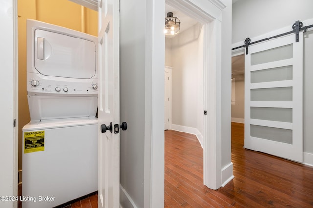 laundry room featuring a barn door, dark hardwood / wood-style floors, and stacked washer and clothes dryer