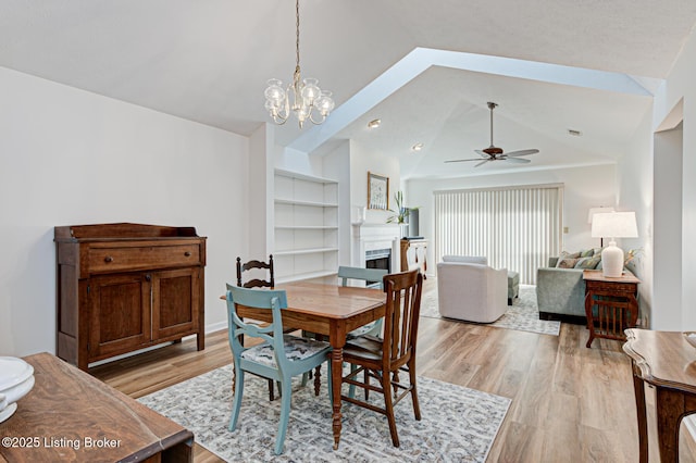 dining space featuring ceiling fan with notable chandelier, lofted ceiling, built in shelves, and light wood-type flooring