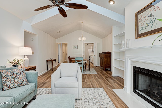 living room featuring ceiling fan with notable chandelier, light hardwood / wood-style floors, a premium fireplace, and built in shelves