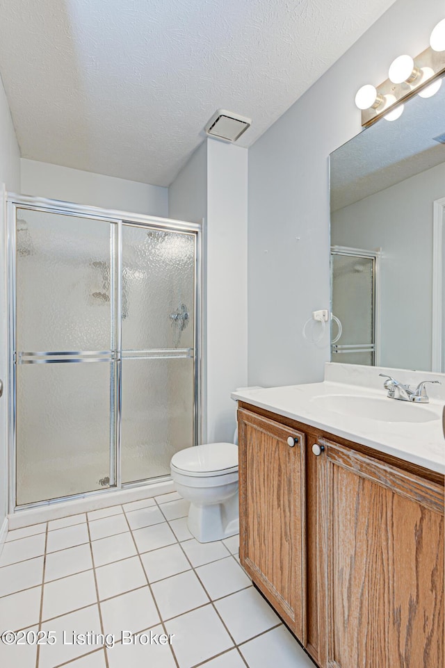 bathroom featuring tile patterned flooring, toilet, vanity, a shower with shower door, and a textured ceiling