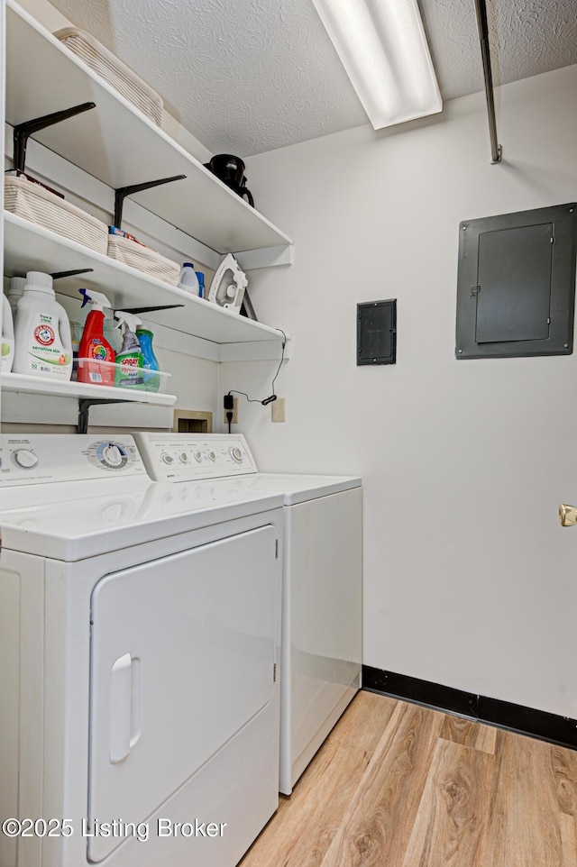 laundry area featuring a textured ceiling, washing machine and clothes dryer, electric panel, and light hardwood / wood-style flooring