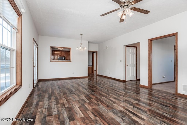 unfurnished living room featuring ceiling fan with notable chandelier, a wealth of natural light, and dark hardwood / wood-style flooring