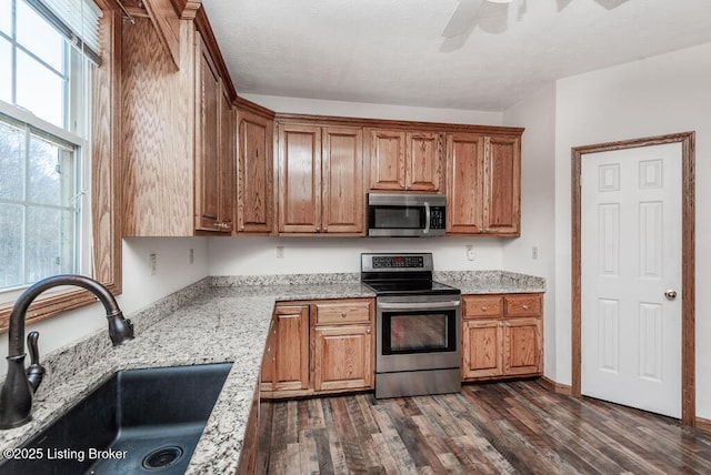 kitchen featuring appliances with stainless steel finishes, dark hardwood / wood-style flooring, ceiling fan, sink, and light stone counters