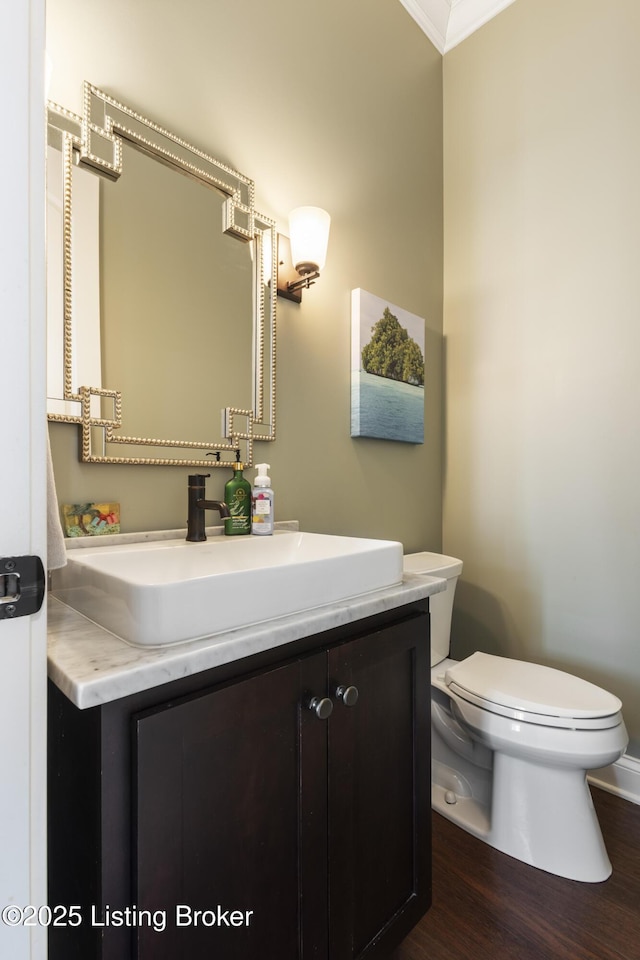 bathroom featuring wood-type flooring, ornamental molding, vanity, and toilet