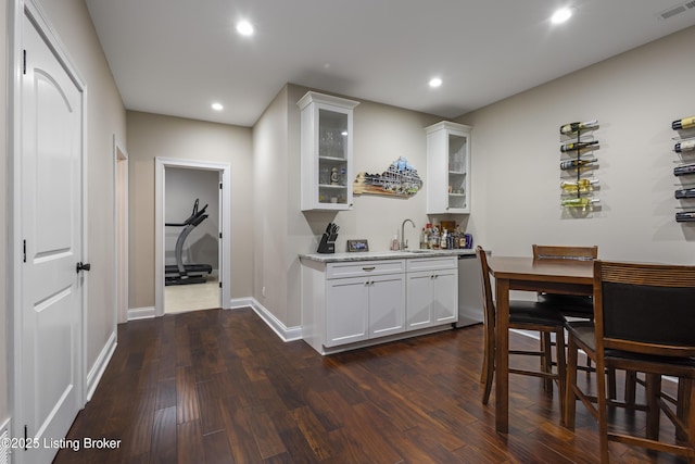 bar featuring sink, white cabinets, dishwasher, light stone counters, and dark wood-type flooring