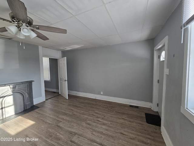 unfurnished living room featuring a drop ceiling, ceiling fan, and dark hardwood / wood-style flooring