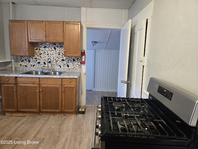 kitchen with sink, tasteful backsplash, light hardwood / wood-style floors, and stainless steel range with gas stovetop