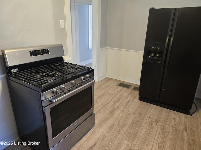 kitchen with black fridge with ice dispenser, light hardwood / wood-style flooring, and gas range