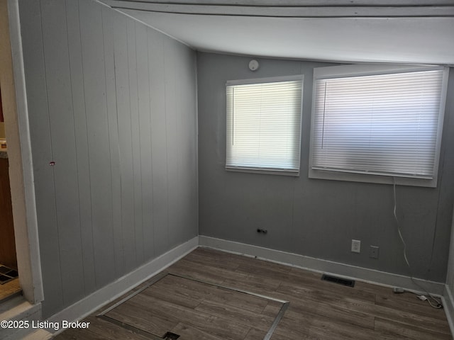 unfurnished room featuring dark hardwood / wood-style floors, wooden walls, and vaulted ceiling