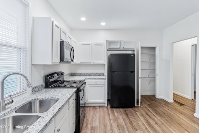 kitchen featuring white cabinetry, sink, light stone counters, light hardwood / wood-style flooring, and black appliances