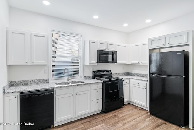 kitchen with light stone countertops, light wood-type flooring, sink, black appliances, and white cabinets