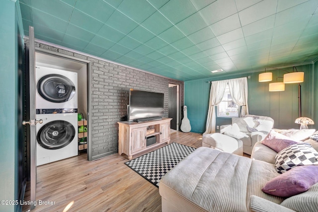 living room with stacked washer and dryer, brick wall, and light wood-type flooring