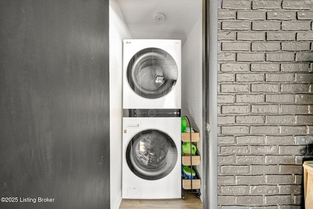 laundry area featuring hardwood / wood-style flooring, brick wall, and stacked washing maching and dryer