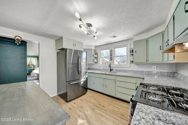 kitchen with stainless steel fridge, green cabinets, light wood-type flooring, stove, and sink