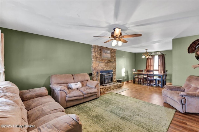 living room with ceiling fan with notable chandelier, hardwood / wood-style flooring, and a wood stove