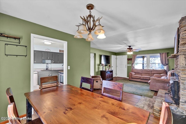 dining room with ceiling fan with notable chandelier, wood-type flooring, and sink