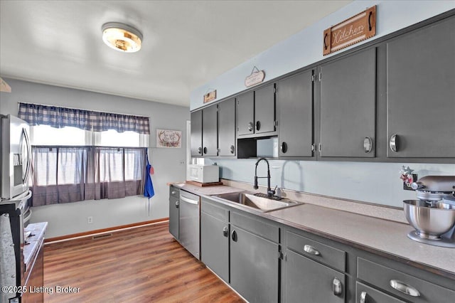 kitchen featuring hardwood / wood-style floors, appliances with stainless steel finishes, gray cabinets, and sink