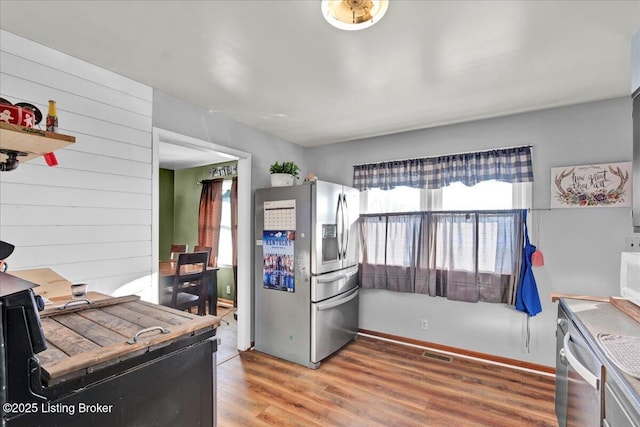 kitchen with wood-type flooring, wooden walls, and appliances with stainless steel finishes