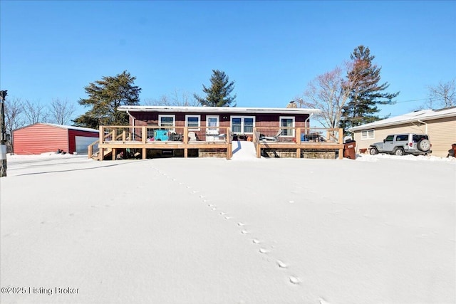 snow covered back of property with a garage and a wooden deck