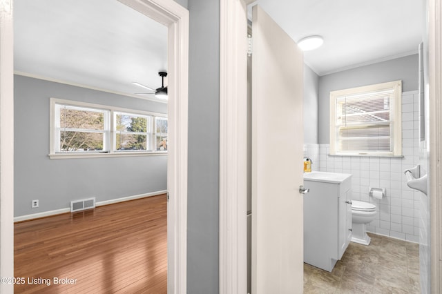 bathroom with tile walls, ornamental molding, ceiling fan, and vanity