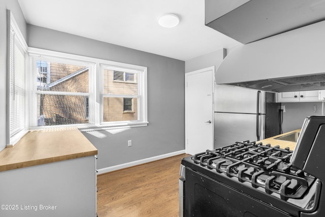 kitchen featuring black gas range, extractor fan, white cabinetry, and light hardwood / wood-style flooring