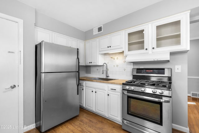 kitchen with appliances with stainless steel finishes, dark wood-type flooring, decorative backsplash, white cabinets, and sink