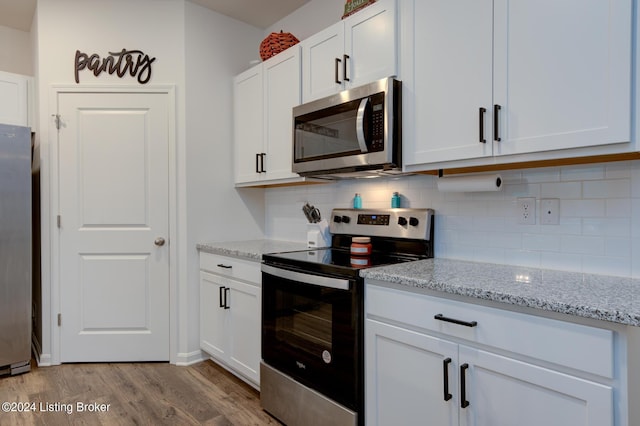 kitchen featuring white cabinets, light hardwood / wood-style flooring, tasteful backsplash, light stone counters, and stainless steel appliances