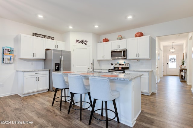 kitchen featuring light wood-type flooring, backsplash, stainless steel appliances, white cabinets, and an island with sink