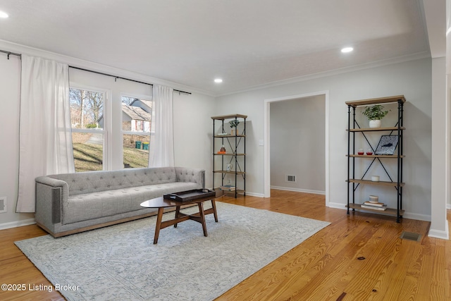 living room with crown molding, visible vents, and light wood finished floors