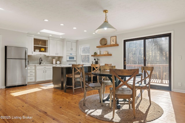 dining room featuring light wood-type flooring, recessed lighting, a skylight, crown molding, and baseboards