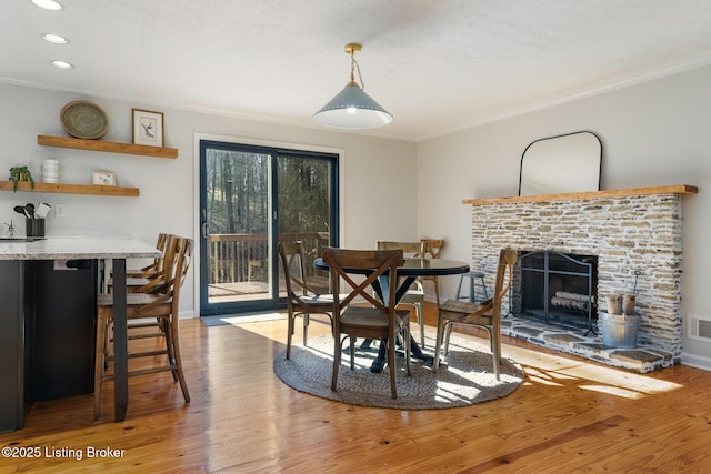 dining room with visible vents, a fireplace with raised hearth, crown molding, baseboards, and wood finished floors