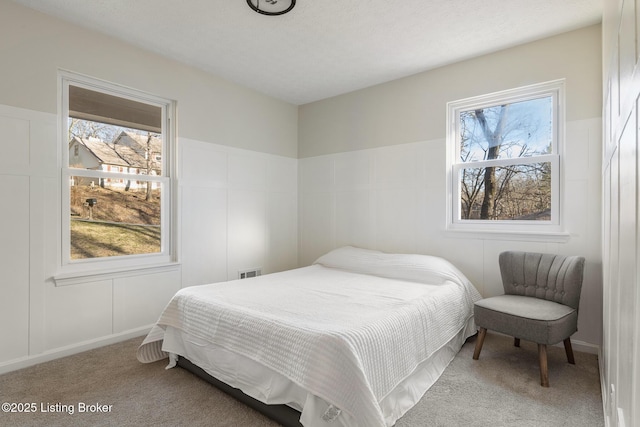 bedroom featuring visible vents, multiple windows, carpet, and a decorative wall