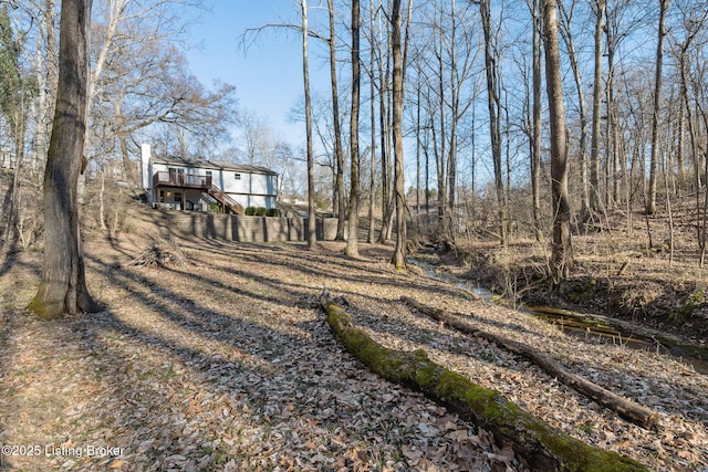 view of yard with a wooden deck, stairs, and a view of trees