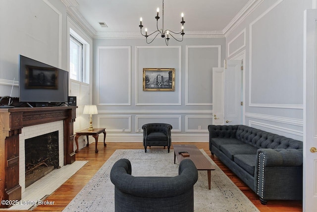 living room with hardwood / wood-style floors, an inviting chandelier, a brick fireplace, and ornamental molding