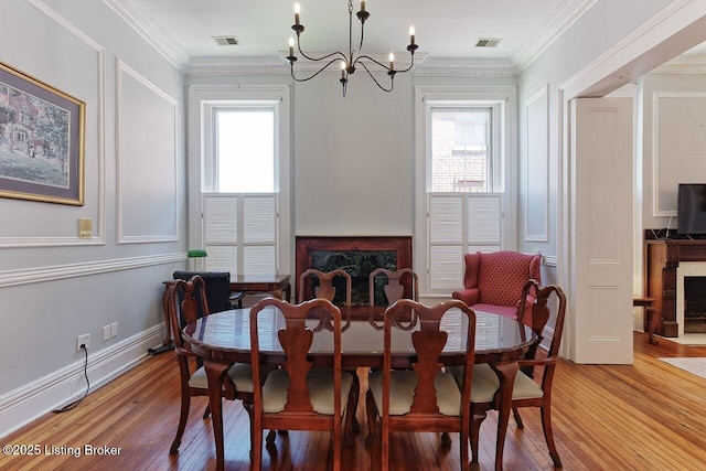 dining area with a fireplace, wood-type flooring, a chandelier, and ornamental molding