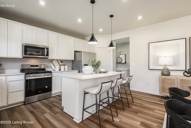 kitchen with a center island, decorative light fixtures, white cabinetry, wood-type flooring, and stainless steel appliances