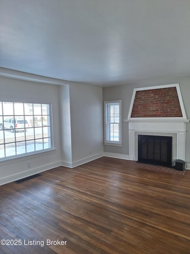 unfurnished living room featuring a brick fireplace, dark wood finished floors, visible vents, and baseboards