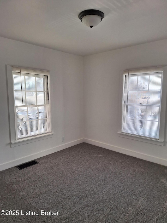 unfurnished room with visible vents, dark carpet, and baseboards