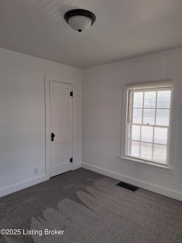 spare room with visible vents, dark carpet, and baseboards