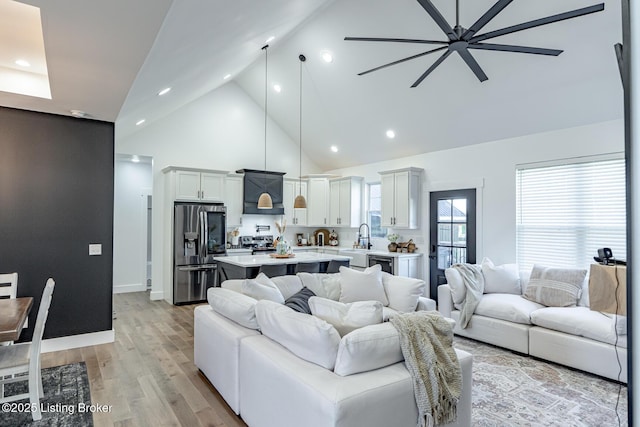 living room with light hardwood / wood-style floors, high vaulted ceiling, ceiling fan, and sink