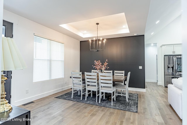 dining area with a notable chandelier, light hardwood / wood-style floors, and a raised ceiling