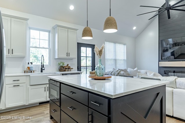 kitchen with sink, hanging light fixtures, light hardwood / wood-style flooring, vaulted ceiling, and white cabinets