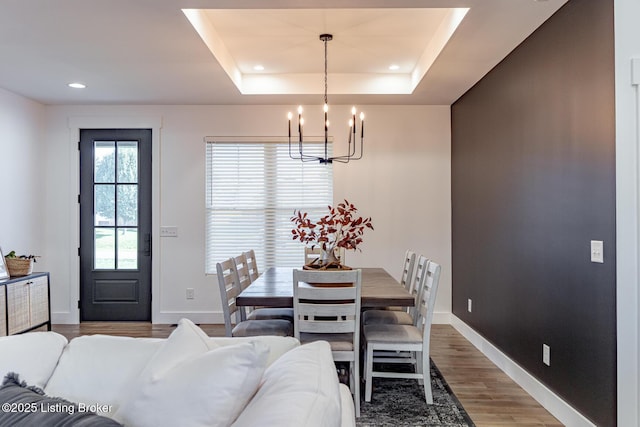 dining area featuring hardwood / wood-style floors, an inviting chandelier, and a raised ceiling