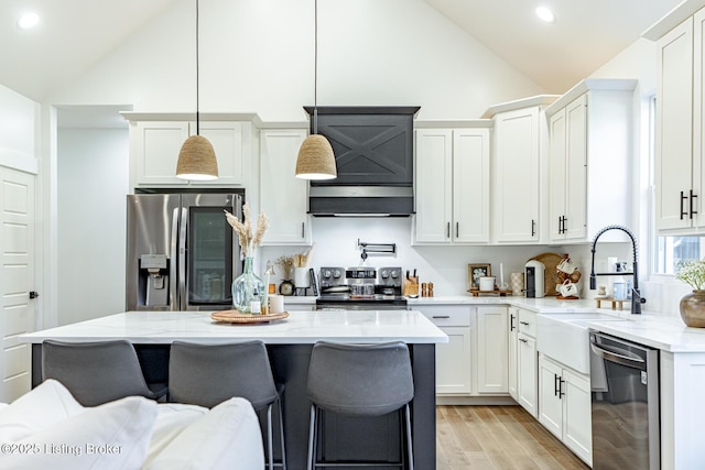 kitchen with lofted ceiling, white cabinets, hanging light fixtures, appliances with stainless steel finishes, and light stone counters