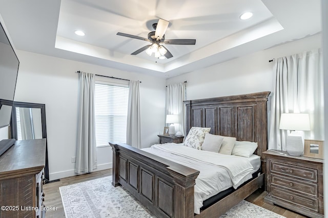 bedroom featuring light wood-type flooring, a tray ceiling, and ceiling fan