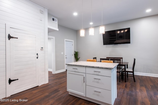 kitchen featuring a center island, white cabinets, dark hardwood / wood-style floors, light stone countertops, and decorative light fixtures