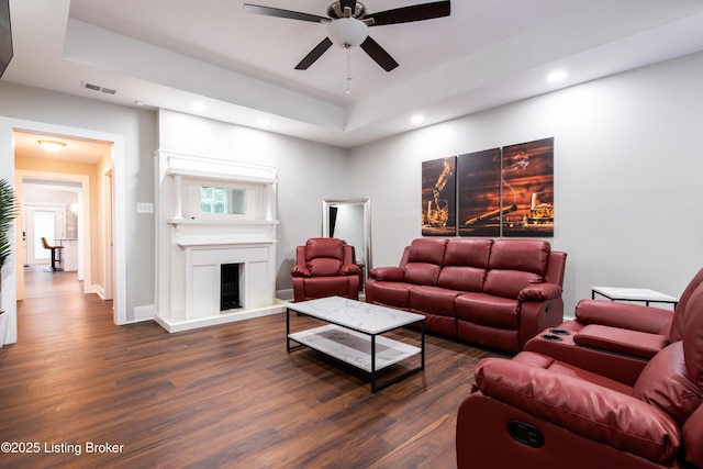 living room with dark hardwood / wood-style flooring, a raised ceiling, and ceiling fan