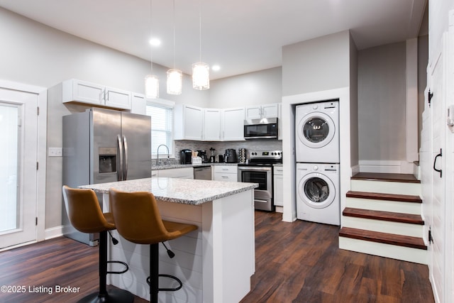 kitchen with appliances with stainless steel finishes, stacked washing maching and dryer, white cabinetry, and pendant lighting